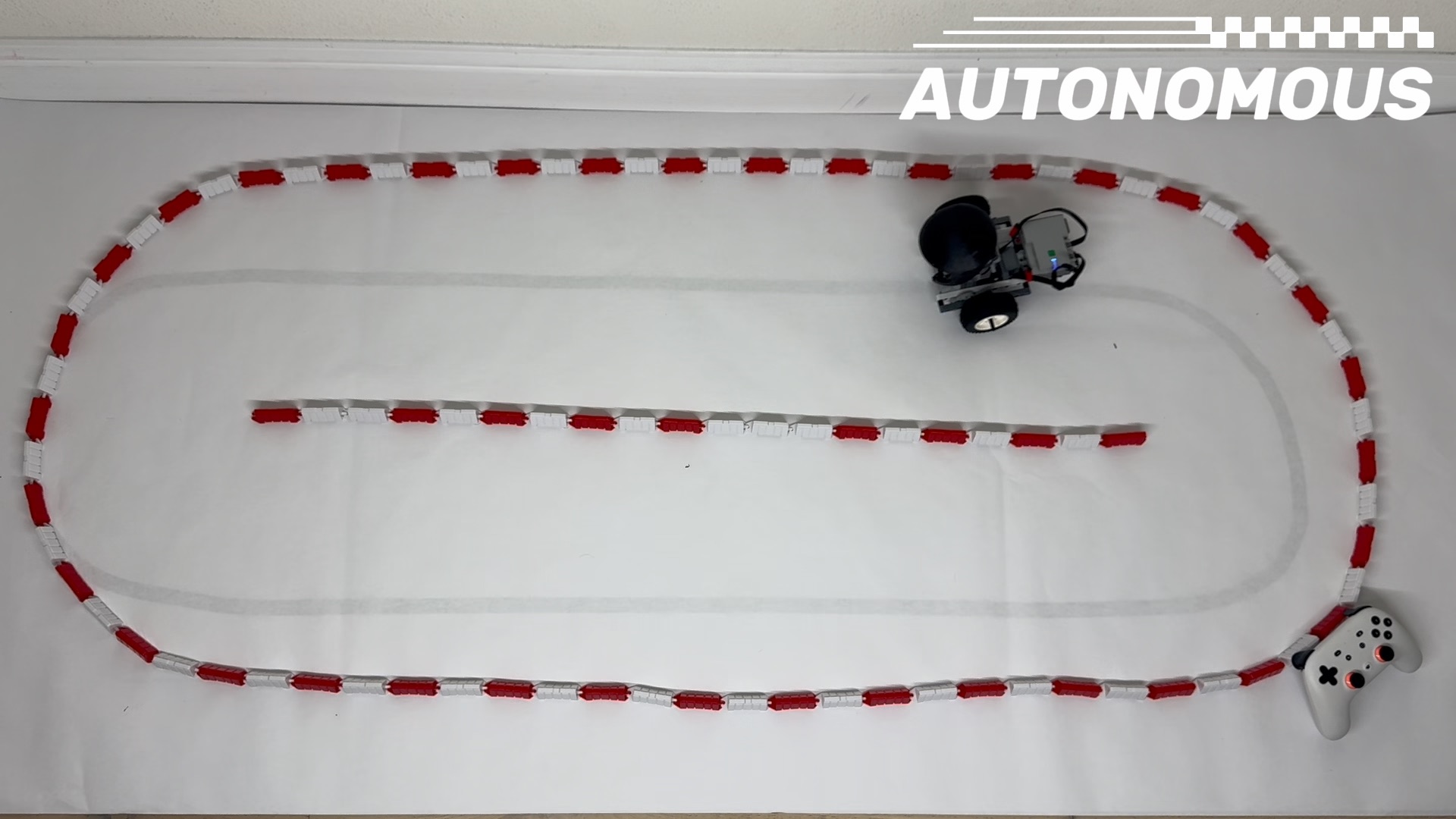 Stack Chan driving inside a red-and-white LEGO guardrail course during a supervised policy trial