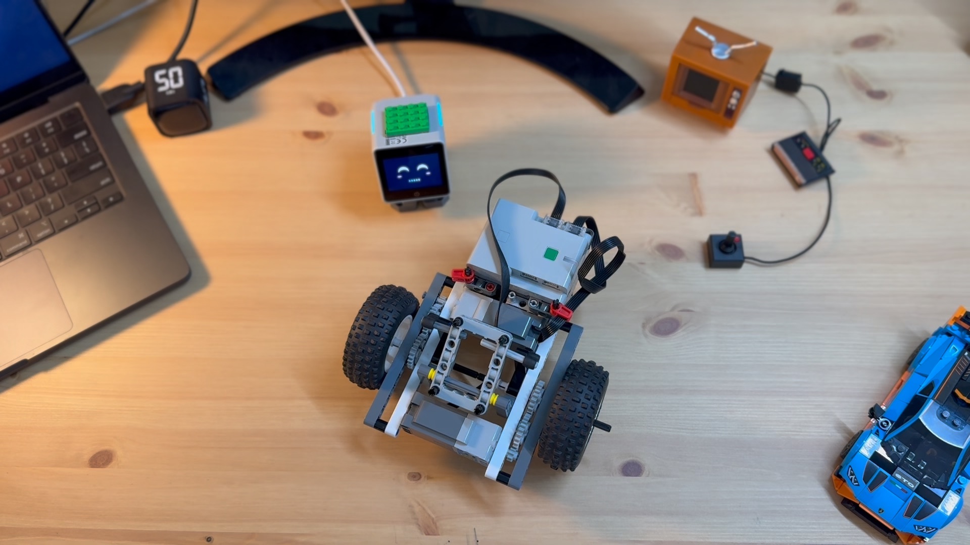 A LEGO two-wheel chassis, hub, and Stack Chan head laid out on a workbench before assembly