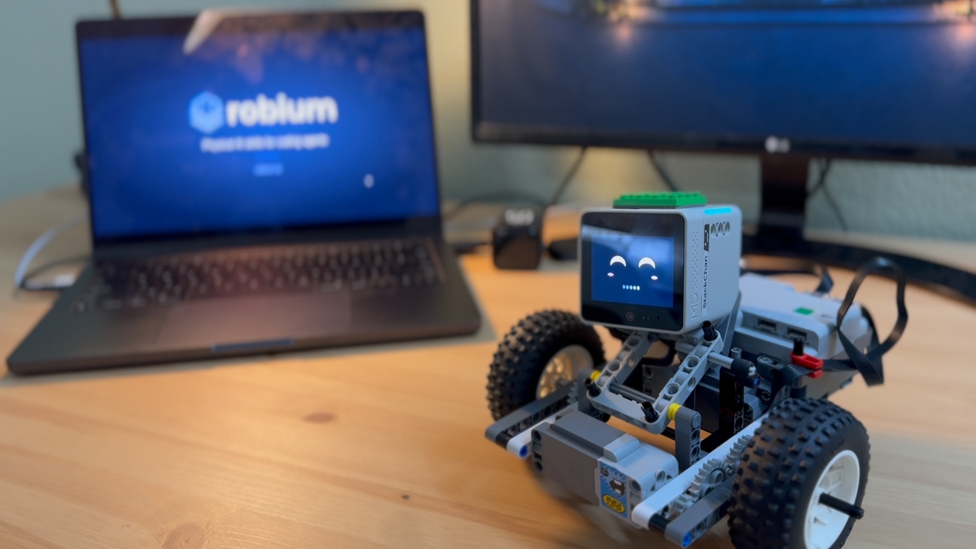 The assembled Stack Chan robot on its LEGO car beside a laptop showing Robium
